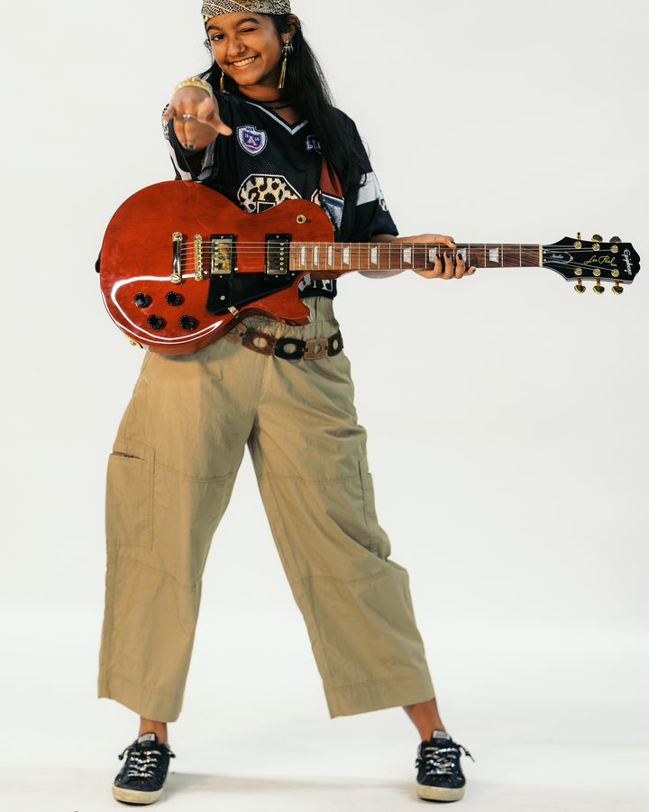 Anya winking and pointing at the camera, red electric guitar in hand